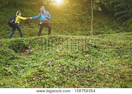 Traveler helping young woman to clime up the hill