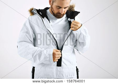 Serious attractive young man zipping up his snowboarding white jacket over unlabeled white t-shirt isolated on white