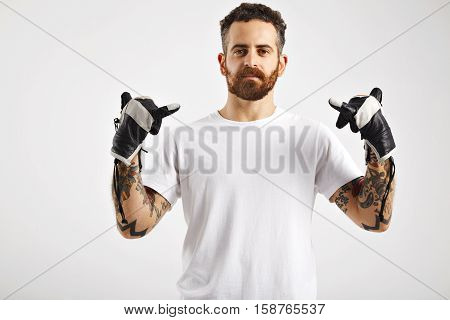 Handsome tattooed and bearded man wearing an unlabeled cotton t-shirt gesturing with his hands in black and white leather snowboarding gloves on white background