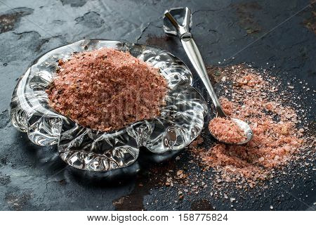 Special pink Adygei salt with spices (Russia) in glass plate and spoon on a dark textured background. Prepared according to the old recipe with garlic and spices. Useful economically spent