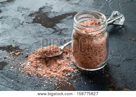 Special pink Adygei salt with spices (Russia) in a glass jar and spoon on a dark textured background. Prepared according to the old recipe with garlic and spices. Useful economically spent