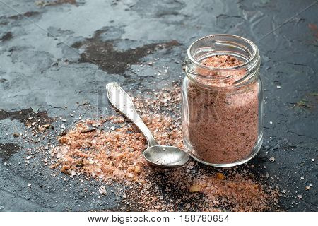 Special pink Adygei salt with spices (Russia) in a glass jar and spoon on a dark textured background. Prepared according to the old recipe with garlic and spices. Useful economically spent