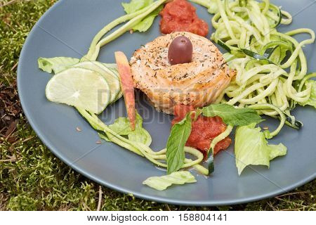 Red fish roll with shredded and sliced vegetables and fruits on plate.