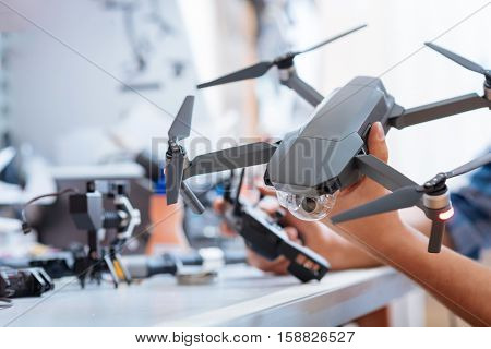 Use it properly. Close up of mans hands holding drone propeller and remore controller while testing the mechanism and sitting in a workroom.