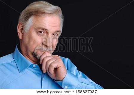 Have a point. Portrait of senior man smiling and loooking at camera keeping his hand on the beard, isolated on black background