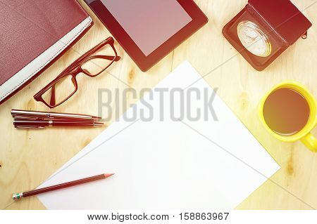 Office table desk top view with tablet PCa cup of coffee pen pencil glasses clock book and blank paper on wooden background. Vintage warm tone effect