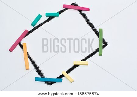 The black frame on a white background, painted wax crayons on the edges of multicolored chalk. Children's creativity. Colorful chalk. Space for text, letters, words. Education, to develop the child.