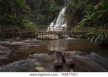 Motion blurred water of Pa Dok Siew Waterfall (Rak Jung waterfall )with trekking shoes as a foreground beautiful waterfall in deep forest Doi Inthanon national park. Rainy season Chiangmai , Thailand