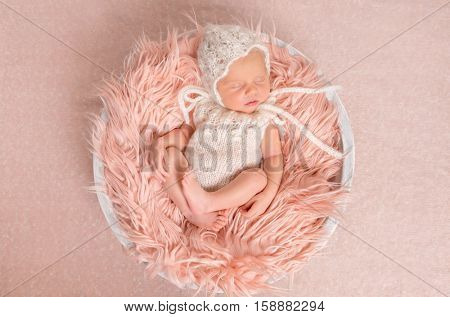 sweet newborn girl in white romper sleeping on round cot with fluffy blanket, top view