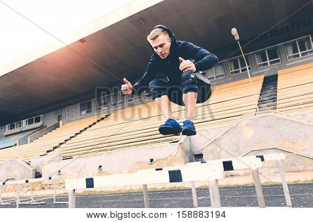 Young athlete jumping over a hurdle during a workout on a treadmill at the old stadium