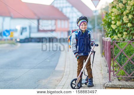 Active school kid boy in safety helmet riding with his scooter in the city. Happy child in colorful clothes biking on way to school. Safe way for kids outdoors to school.