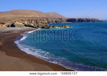 View on the beach Playa de Ajuy with a single person enjoying the ocean on the Canary island Fuerteventura Spain.