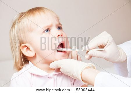 Pediatrician examines sitting child using wooden tongue depressor to check girl's sore throat