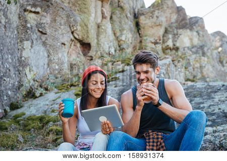 Portrait of a smiling young couple having a break from hiking and using tablet computer