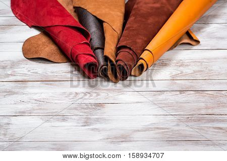 Brightly colored leather in rolls on the white wooden background. Leather craft. Copy space.