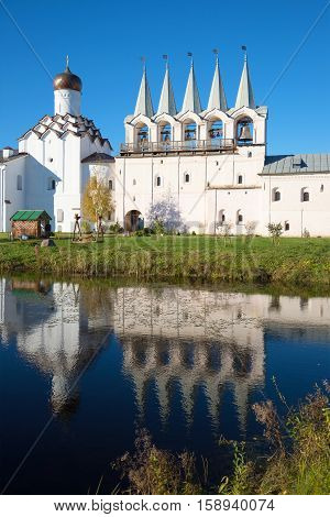 The old bell tower of the Tikhvin assumption monastery and its reflection in the monastery pond, October evening. Tikhvin, Russia