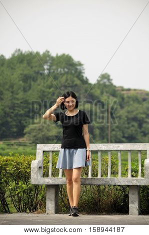 A chinese woman fixing her hair as she walks away from a stone bench in the Wuyishan or Mount Wuyi scenic area in Fujian province China.