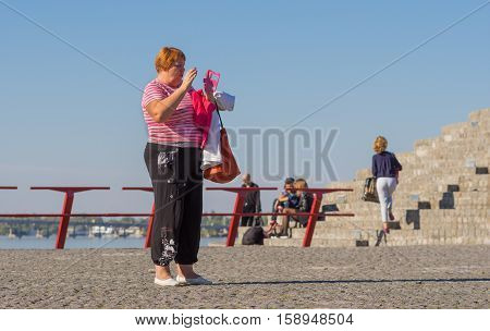 DNEPR, UKRAINE - OCTOBER 02, 2016:Mature woman talking on cellular using speaker standing on a Dnepr river embankment in center of the Dnepr city at warm and sunny autumnal weekend October 02, 2016