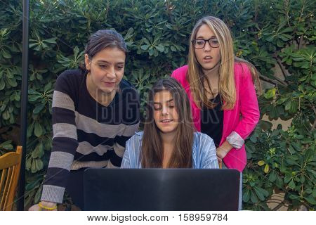 Young entrepreneurs working with a laptop. They are three beautiful Caucasian girls who are creating their company. They work on the terrace of their house.