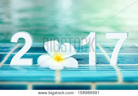 Happy new year card 2017. Number 2017 text with white Plumeria flower on ceramic tile border of swimming pool over bokeh blur water background.