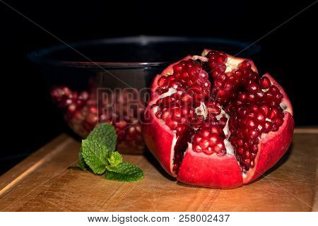 Close Up Of Opened Pomegranate Displayed On Wooden Board With Mint Leaf And Bawl Of Seeds