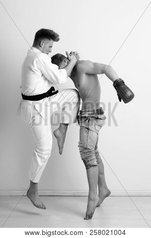 Sport And Combat, Strong Karate Athlete In Kimono With Black Belt Jumping And Kicking Knee At Boxer 