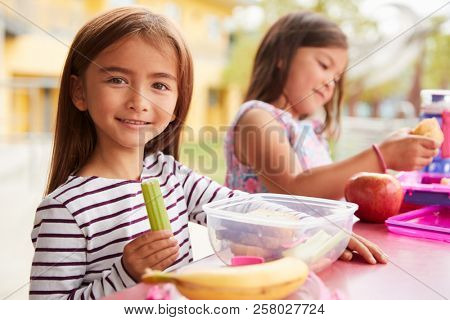 Two young girls eating packed lunches at school, close up