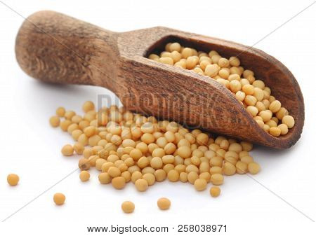 Golden Mustard Seeds In A Wooden Scoop Over White Background