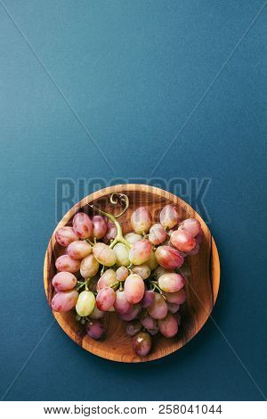 Bunch Of Red Grape On Wooden Plate On Dark Blue Background. Top View With Copy Space.