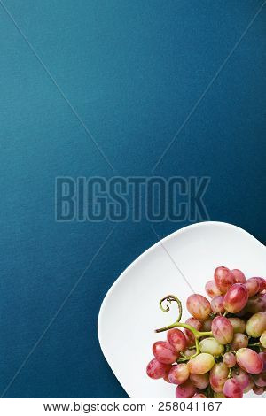 Bunch Of Red Grape On White Plate On Dark Blue Background. With Place For Text.