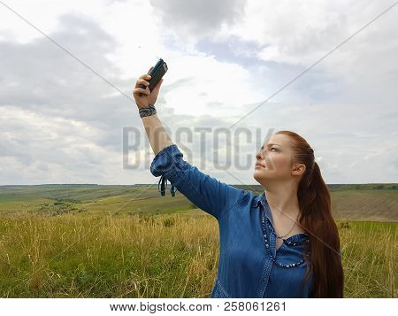 A Young Woman With Red Hair And A Blue Denim Dress Is In The Mountains Outside The City And Is Tryin