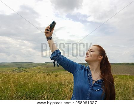 A Young Woman With Red Hair And A Blue Denim Dress Is In The Mountains Outside The City And Is Tryin