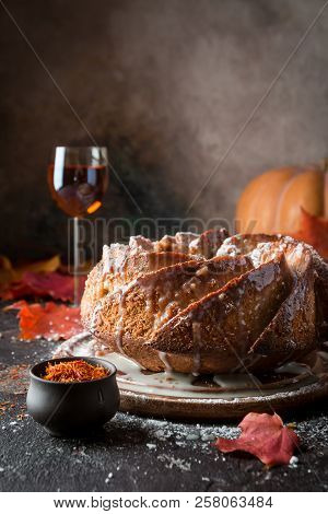 Bundt Cake With Saffron And Rum Covered With White Glaze On Rustic Background With Autumn Decoration