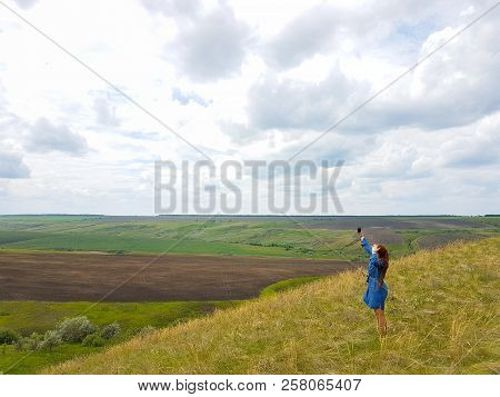 A Young Woman With Red Hair And A Blue Denim Dress Is In The Mountains Outside The City And Is Tryin