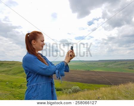 A Young Woman With Red Hair And A Blue Denim Dress Is In The Mountains Outside The City And Is Tryin