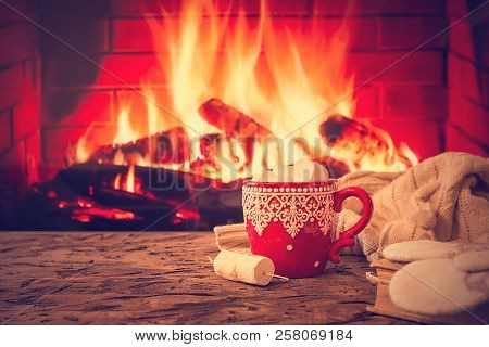 Mug Of Hot Chocolate Or Coffee With Marshmallows In A Red Mug On Vintage Wood Table In Front Of Fire