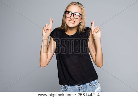 Young Woman Keeps Fingers Crossed, Hopes For Good Luck, Isolated Against Gray Background With Copy S