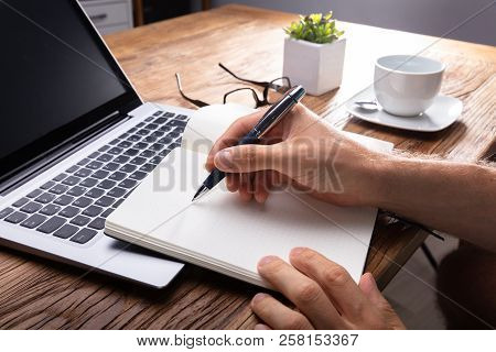 Person's Hand Writing On Black Notebook