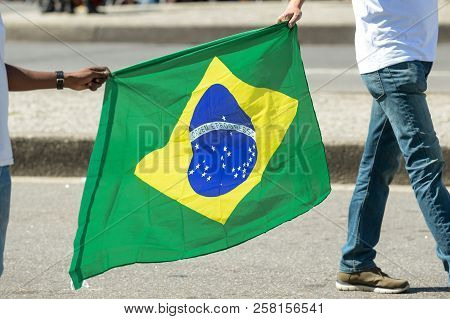 Two People Holding The Brazilian Flag In A Streer