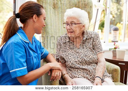 Senior Woman Sitting In Chair And Laughing With Nurse In Retirement Home