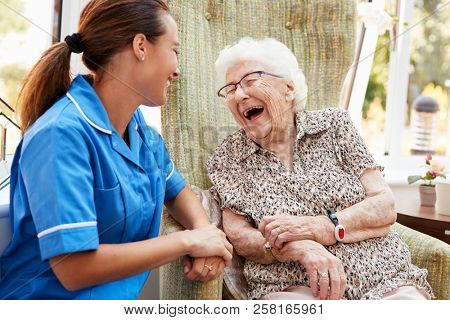Senior Woman Sitting In Chair And Talking With Nurse In Retirement Home