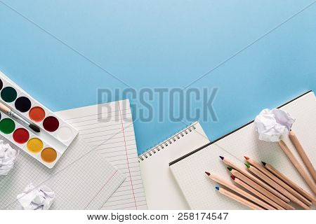 Top View Over A Notebooks, Paints, Pencils And Crumped Papers. Back To School Concept. Office Suppli