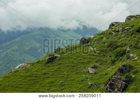A Green Hillside With Rocks And Clouds