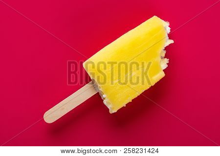 Yellow Popsicle With Some Bites On A Rose Red Background