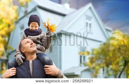 family, real estate and fatherhood concept - happy father carrying son with autumn maple leaves over living house background