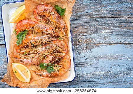 Traditional fried black tiger prawn with lemon as top view in a white casserole on a wooden blue board 
