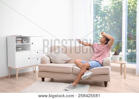 Young Man Suffering From Heat At Home. Air Conditioner Malfunction