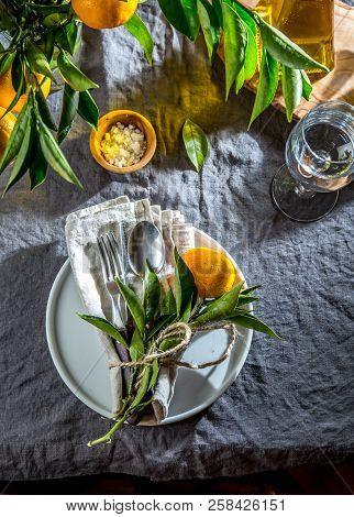 Table Setting With White Plate, Cutlery, Linen Napkin And Orange Tree Branch Decoration On Gray Line