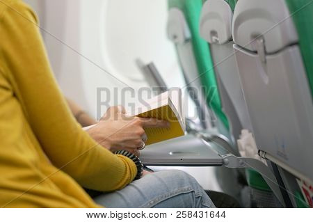 A Young Man Reads A Book On The Plane With His Wife. A Man Traveling By Plane. A Man Reading A Book 