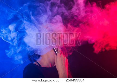 Portrait Of Young Woman In Neon Blue And Red Smoke With Vape Or E-cigarettes